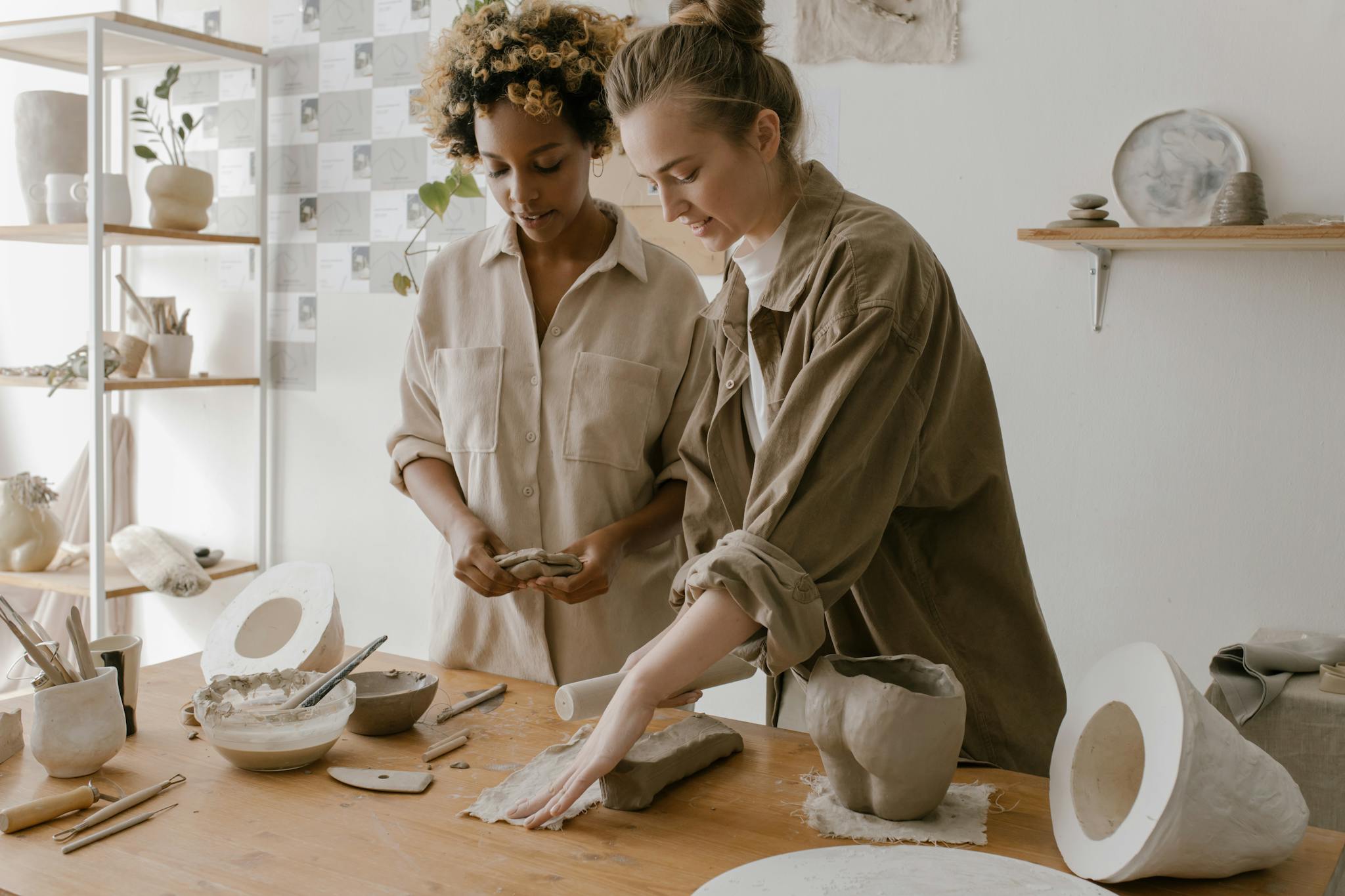 Two women crafting pottery in a creative workshop setting, focused on skill and creativity.