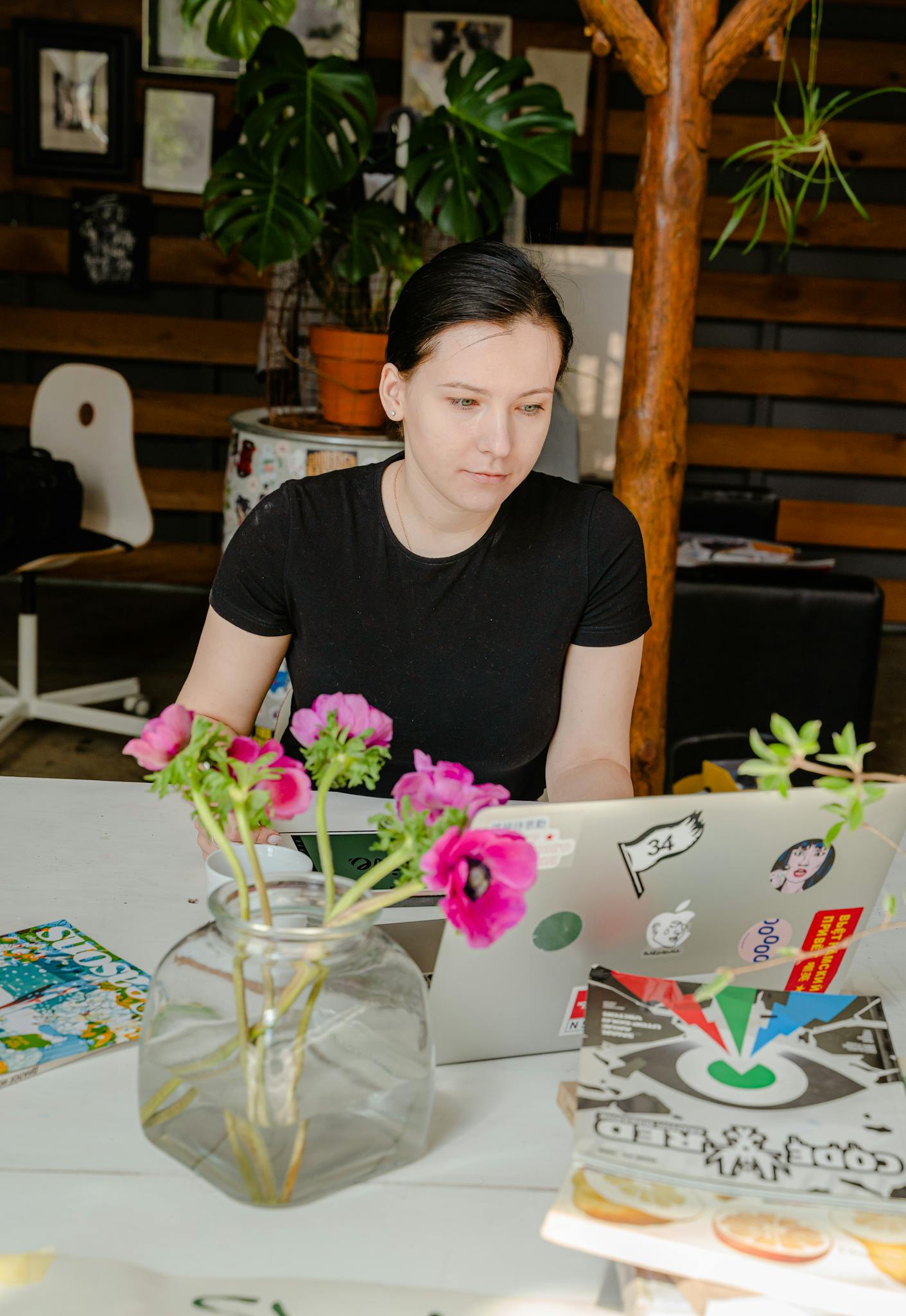 Woman in black shirt working on laptop amidst art materials in a creative indoor space.